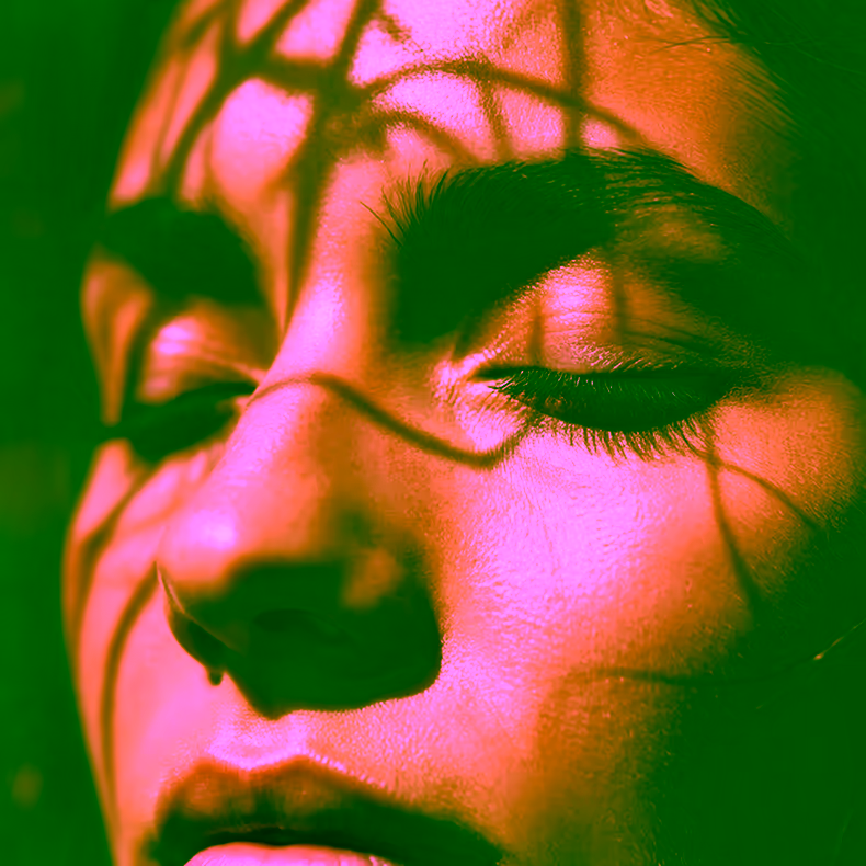 A close-up of a person's face with closed eyes, soft sunlight illuminating their skin. Shadows from nearby branches or leaves create intricate patterns across their face.